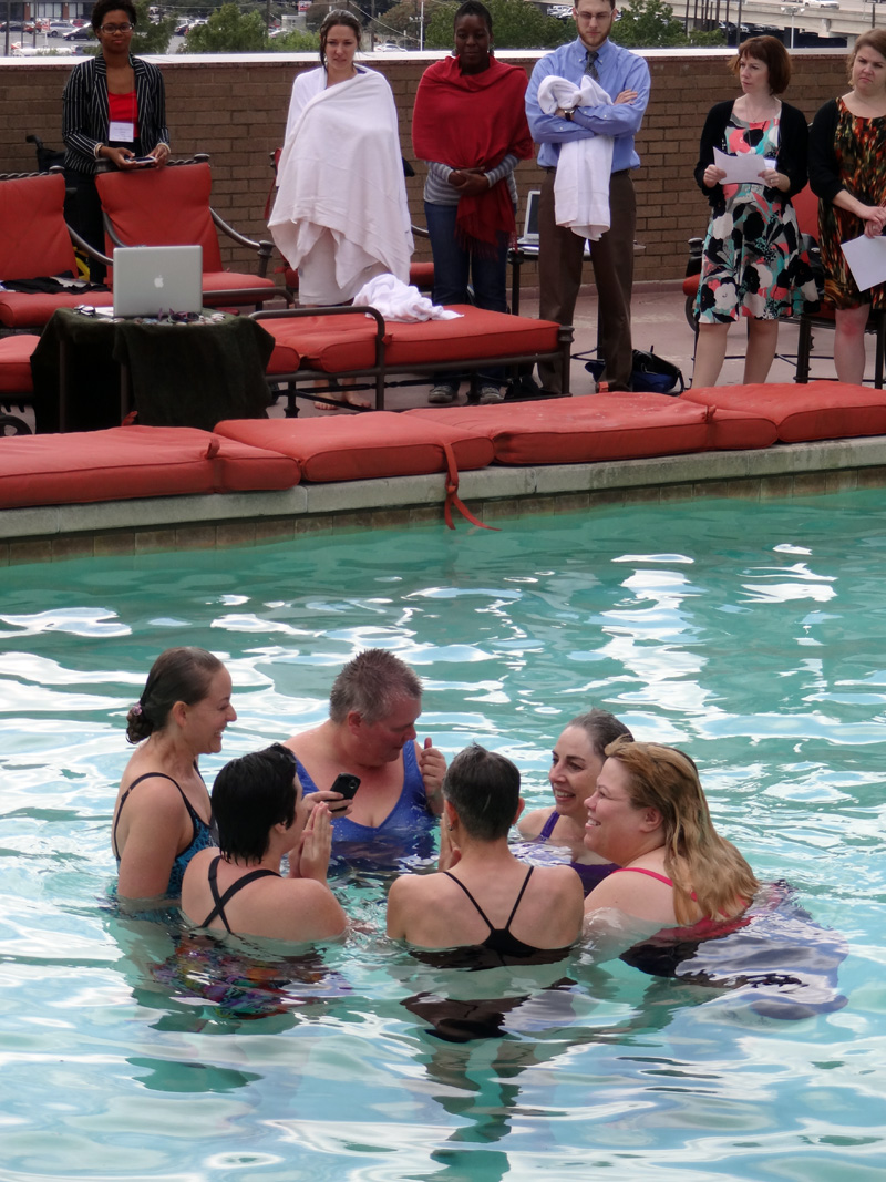 Salamander performance at rooftop pool in Dallas, circle of women in the cold water, people standing at side of pool, reciting poetry and helping swimmers out of the water and warming them up